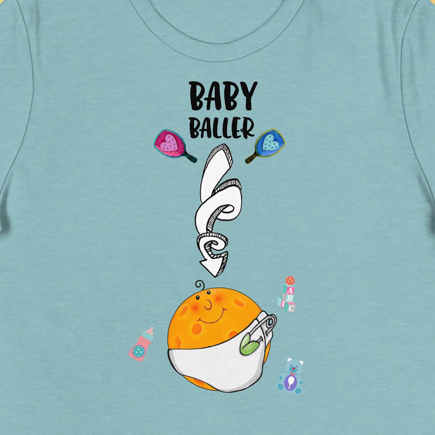 Closeup view of Baby Baller Maternity shirt graphic on front of women's heather blue pickleball tshirt